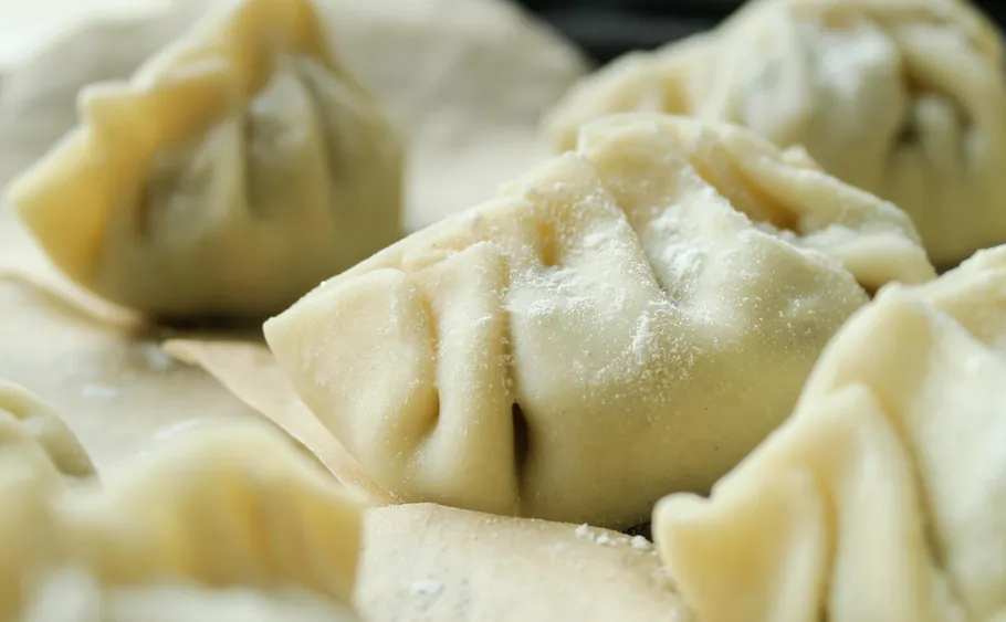 Close-up of uncooked dumplings on parchment paper.