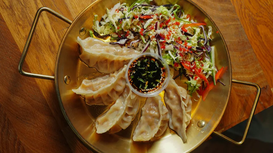 Dumplings with salad and dipping sauce on platter.