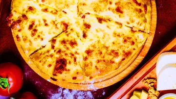 Cheesy pizza on wooden platter with tomatoes nearby.
