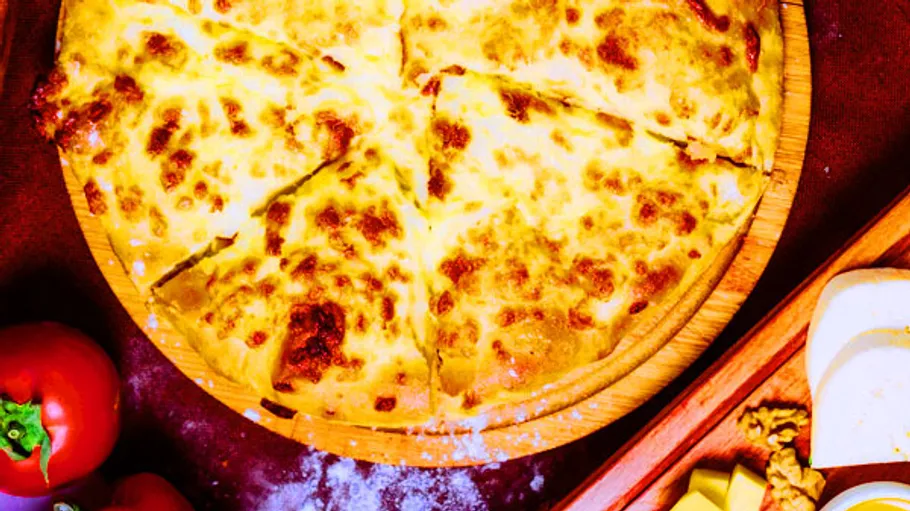 Cheesy pizza on wooden platter with tomatoes nearby.