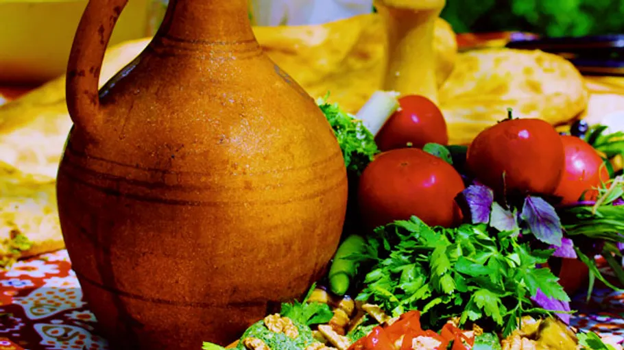 Clay jug on table with vegetables and herbs.