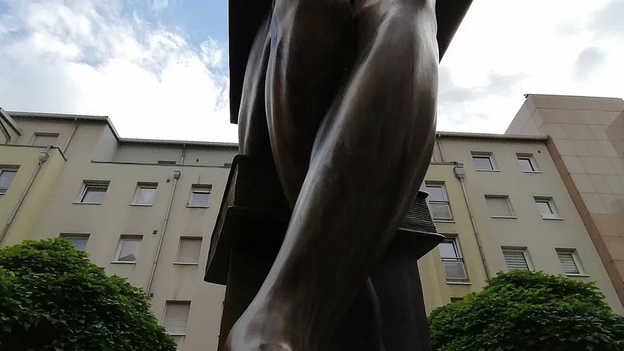 Statue's legs viewed from below, city background.