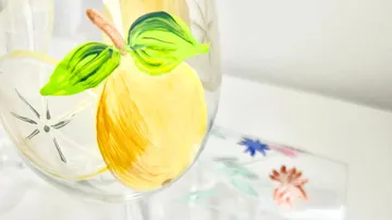 Glas mit gemalter Zitrone und Blättern, Blumenhintergrund.