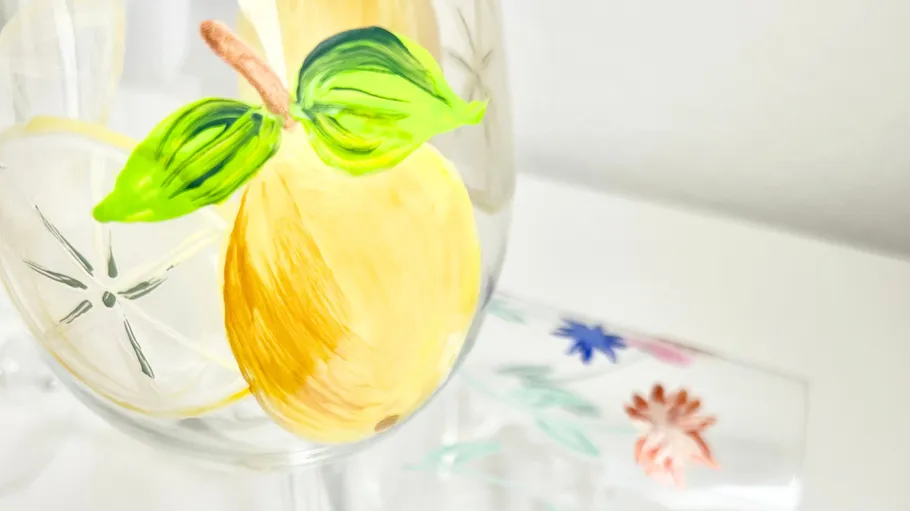 Glass with painted lemon and leaves, floral background.
