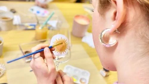 Person painting sun on wine glass indoors.