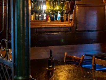 There is a bottle on a brown table, surrounded by darkness and light.
