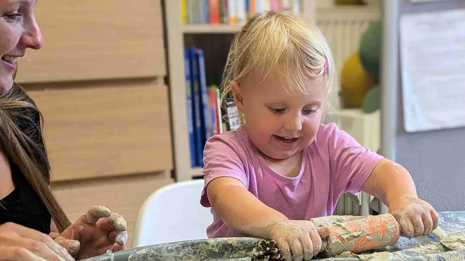 Child playing with dough at table, happy.