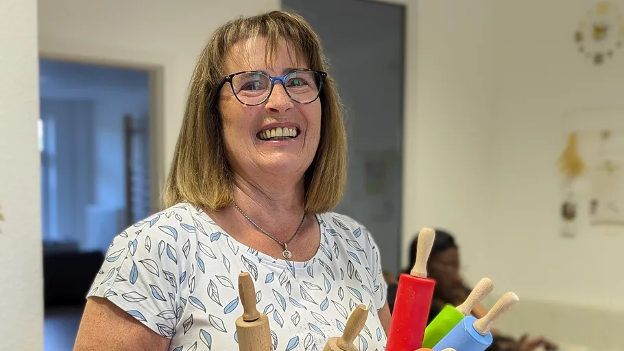 Smiling woman holding colorful rolling pins indoors.