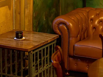 Wooden table with a cup on a trivet, next to a leather chair.