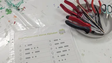 Werkzeuge auf Teller neben Morsecode-Blatt.