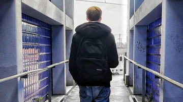 Person walking on a narrow pathway between glass walls.