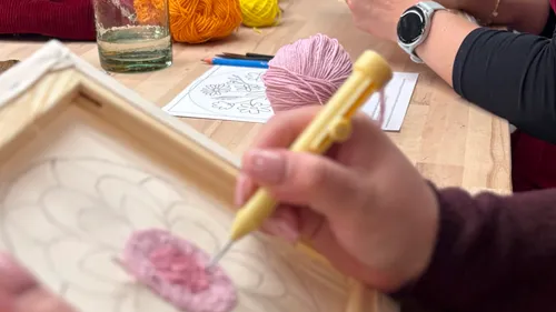 Person punch needling floral design on fabric.