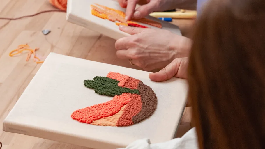 Hände sticken buntes Stoff auf Holztisch.
