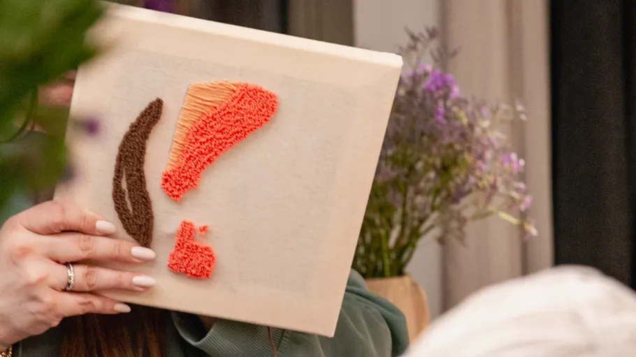 Person holding embroidered canvas in floral setting.