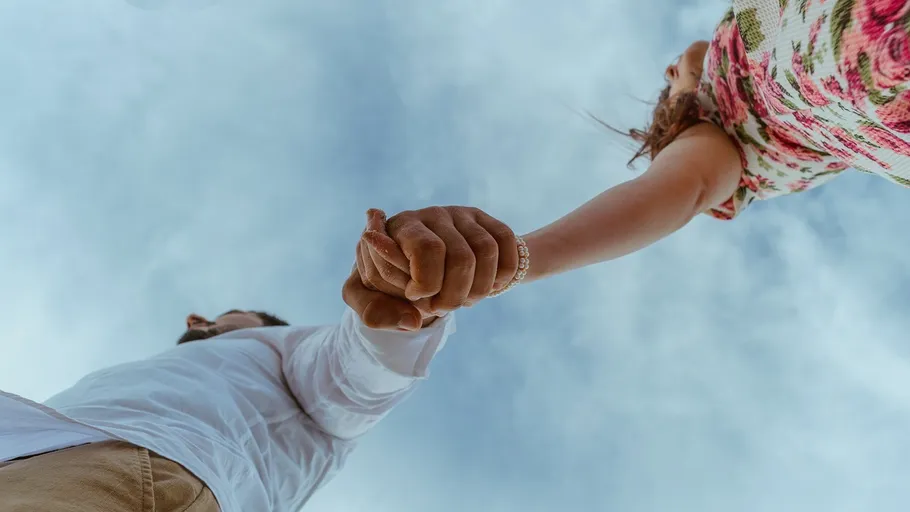 Couple holding hands under blue sky.