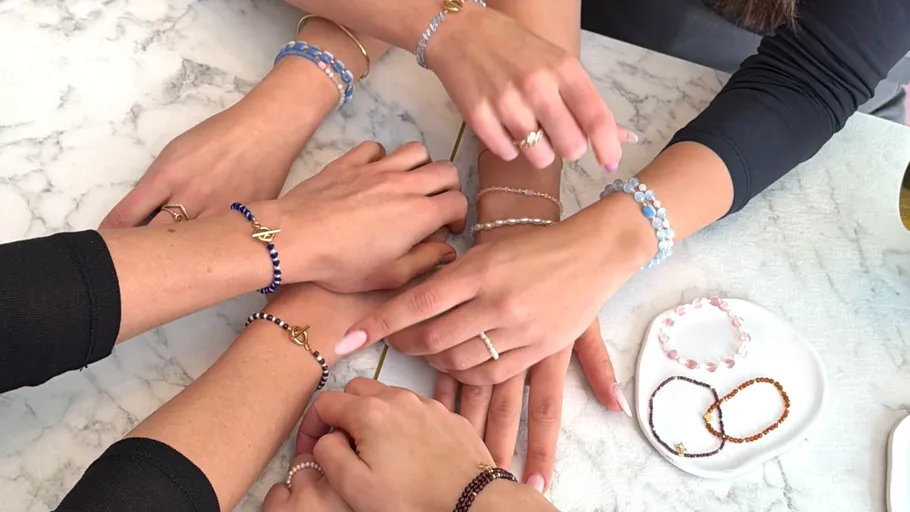 Hands with beaded bracelets on marble table.