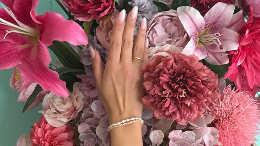 Hand mit Schmuck berührt bunte Blumen.