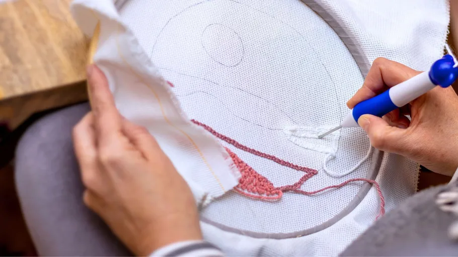 Person embroidering fabric with punch needle tool.