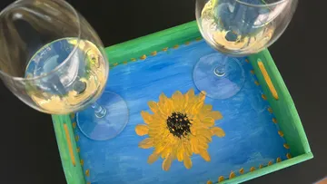 Zwei Weingläser auf sonnenblumenbemaltem Tablett.