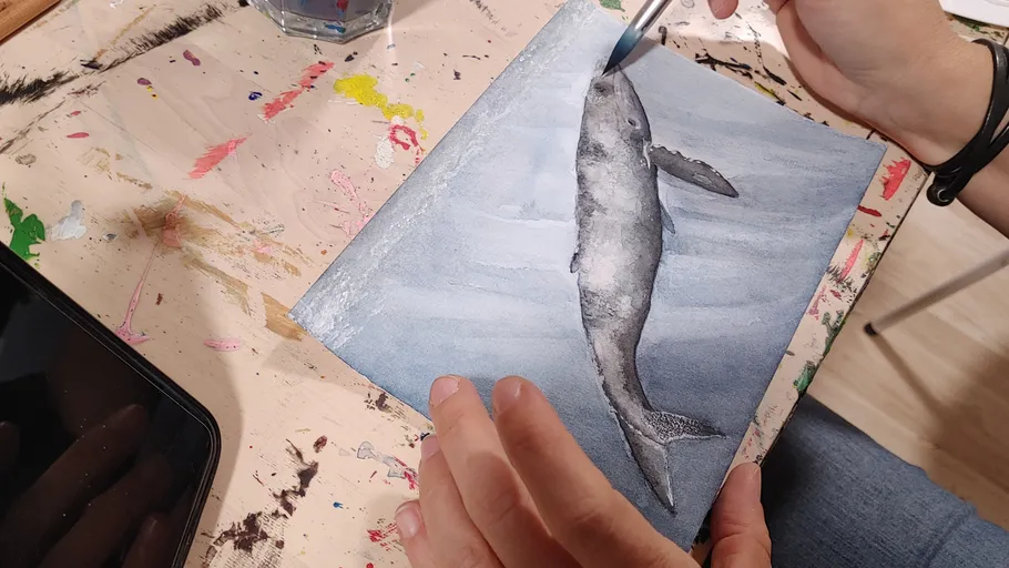 Person painting a whale on watercolor paper.