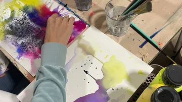 Person malt mit Aquarell auf Holztisch.