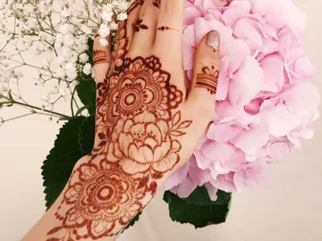 Hands with henna design hold pink flowers in the background