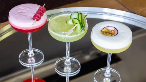 Drei bunte Cocktails auf einem Tisch.