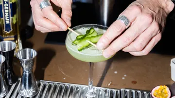 Barkeeper garniert Cocktail mit Gurkenscheiben.
