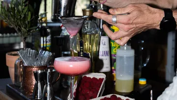 Barkeeper seiht pinken Cocktail in Glas ab.