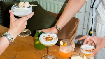 Hände halten Cocktails auf einem Holztisch.
