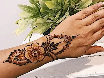 Hand mit Henna-Muster auf dem Unterarm, auf einer Oberfläche.