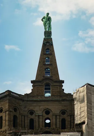 Statue auf hohem Gebäude mit Bogenfenstern.