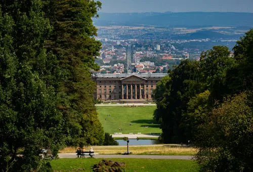 Classical building surrounded by trees, distant city view.