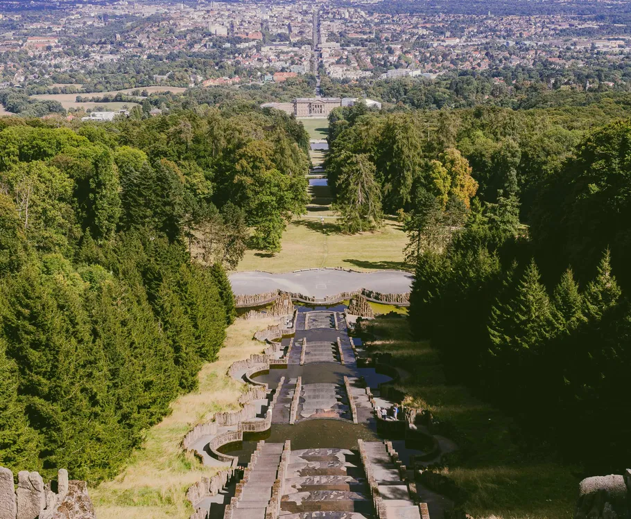 Cascading fountains with trees and distant city view.