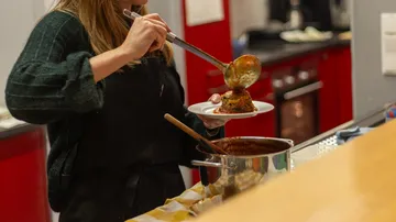 Person serviert Essen aus Topf in Küche.