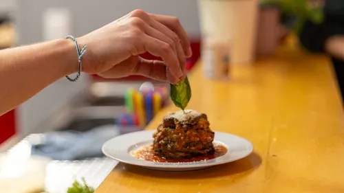 Hand placing basil on dish in kitchen.