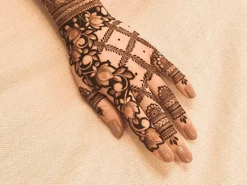 Hand mit kunstvollem Mehndi-Muster auf hellem Hintergrund.