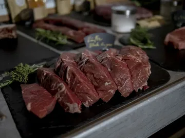 Red meat is lying on a bulletin board surrounded by herbs.