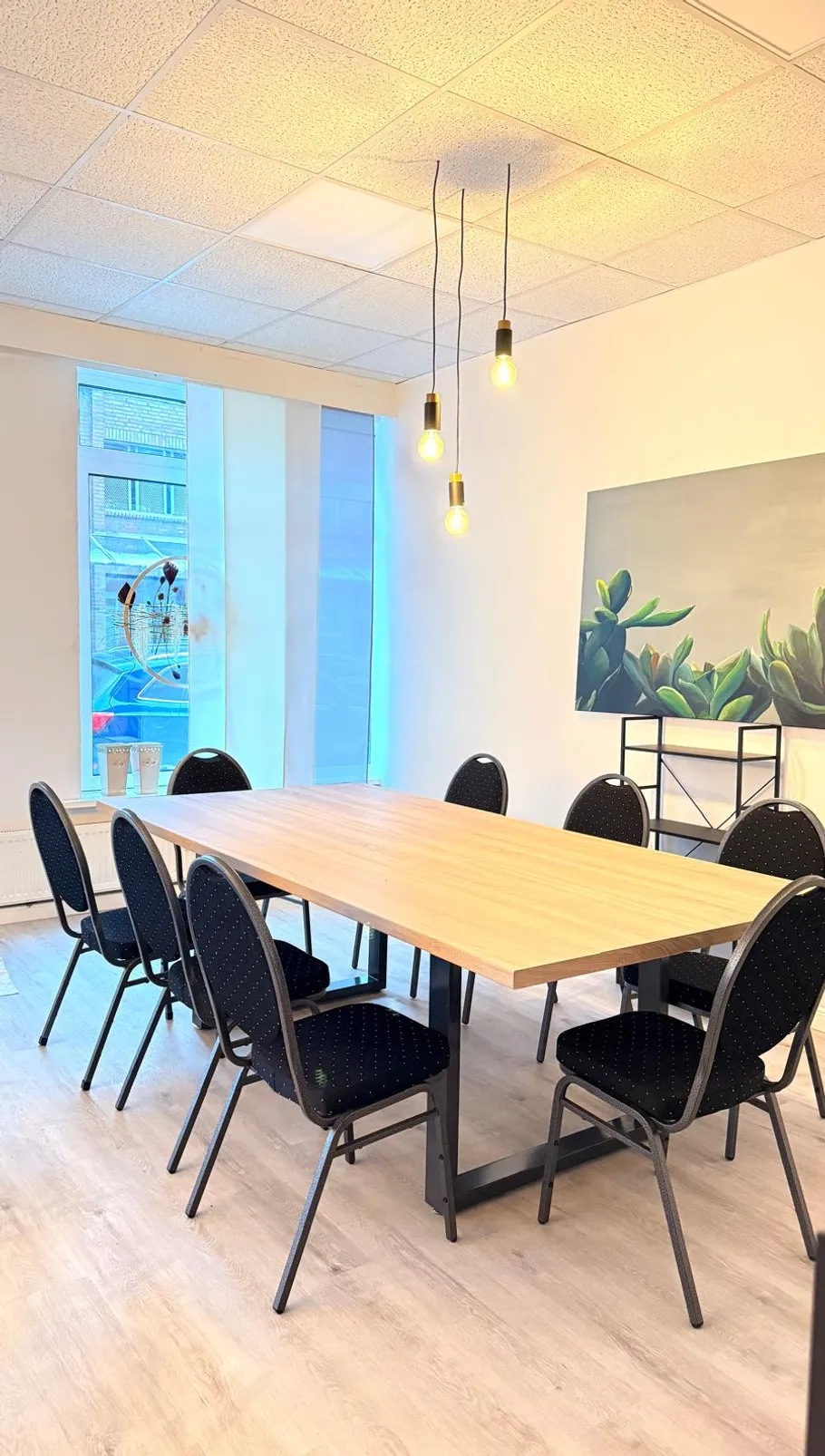 Konferenzraum mit Tisch, Stühlen und Hängelampen.