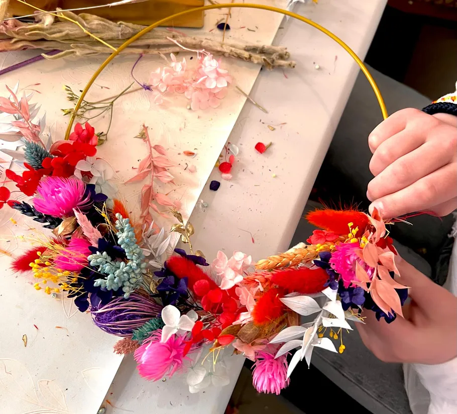 Hands arranging colorful floral wreath on table.
