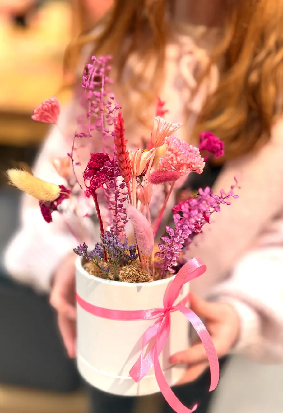 Hands holding colorful dried flower arrangement.