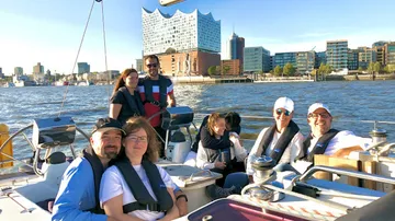 Gruppe segelt auf Boot, Stadtsilhouette im Hintergrund.