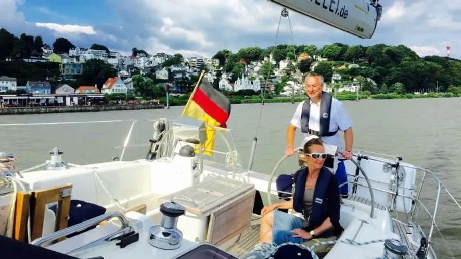 Zwei Personen segeln auf einem Boot am Ufer.