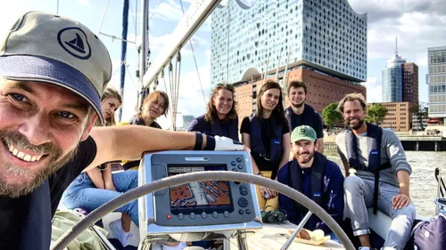 Group sailing, smiling on a boat near modern buildings.