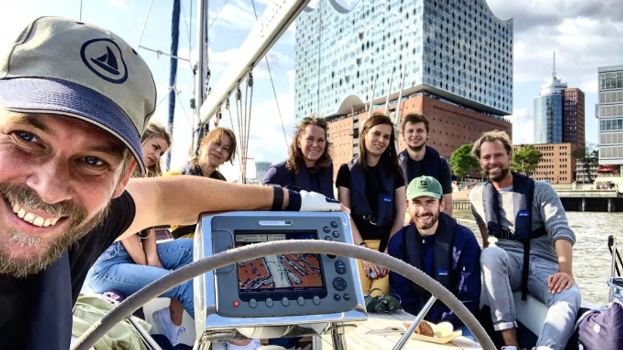Group sailing, smiling on a boat near modern buildings.