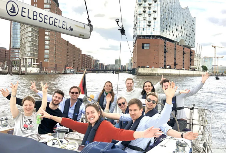 Gruppe auf Segelboot winkt am Stadtgewässer.