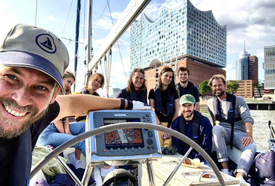 Group on sailboat with cityscape in background.