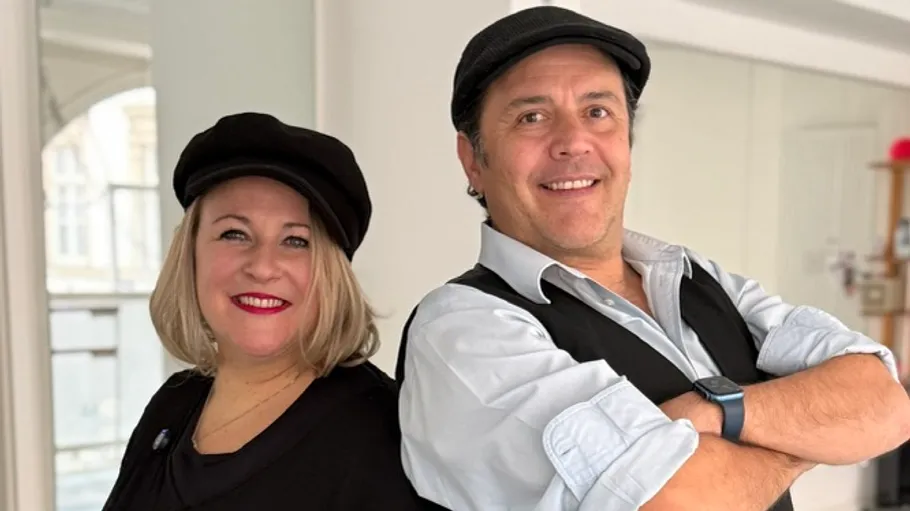 Two people smiling, wearing hats indoors.