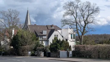 Haus mit Kirchturm und kahlen Bäumen in der Nähe.