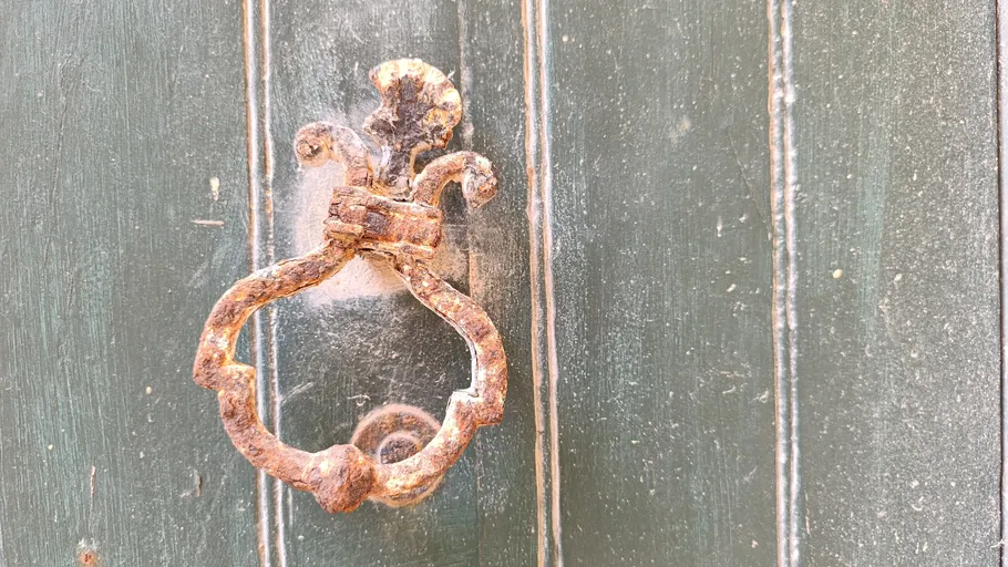 Rustic door knocker on green wooden door.
